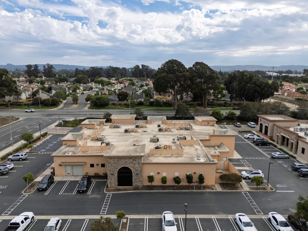 Aerial view of a commercial building with empty parking lot and residential area in background.