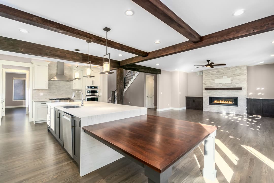 Modern kitchen with island, wooden beams, and spacious living area featuring a fireplace.