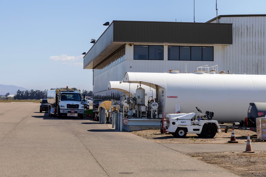Fuel storage tanks and service vehicles outside an airport hangar on a clear day.