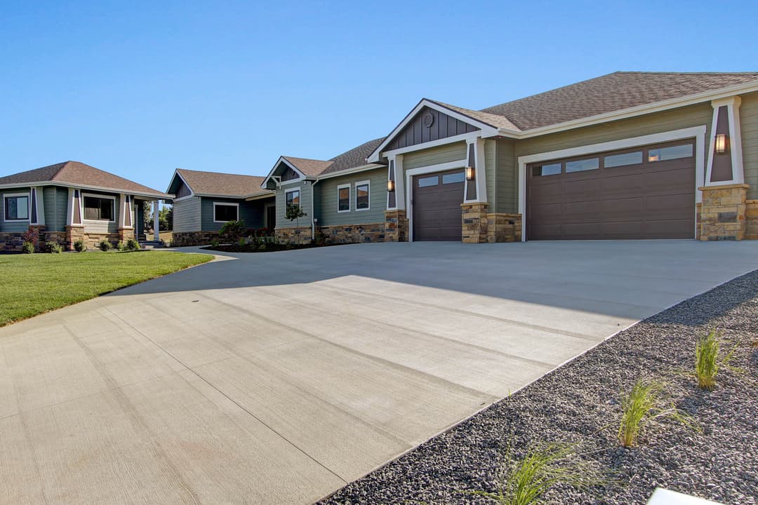 Modern residential homes with stone accents and a spacious driveway under clear blue sky.