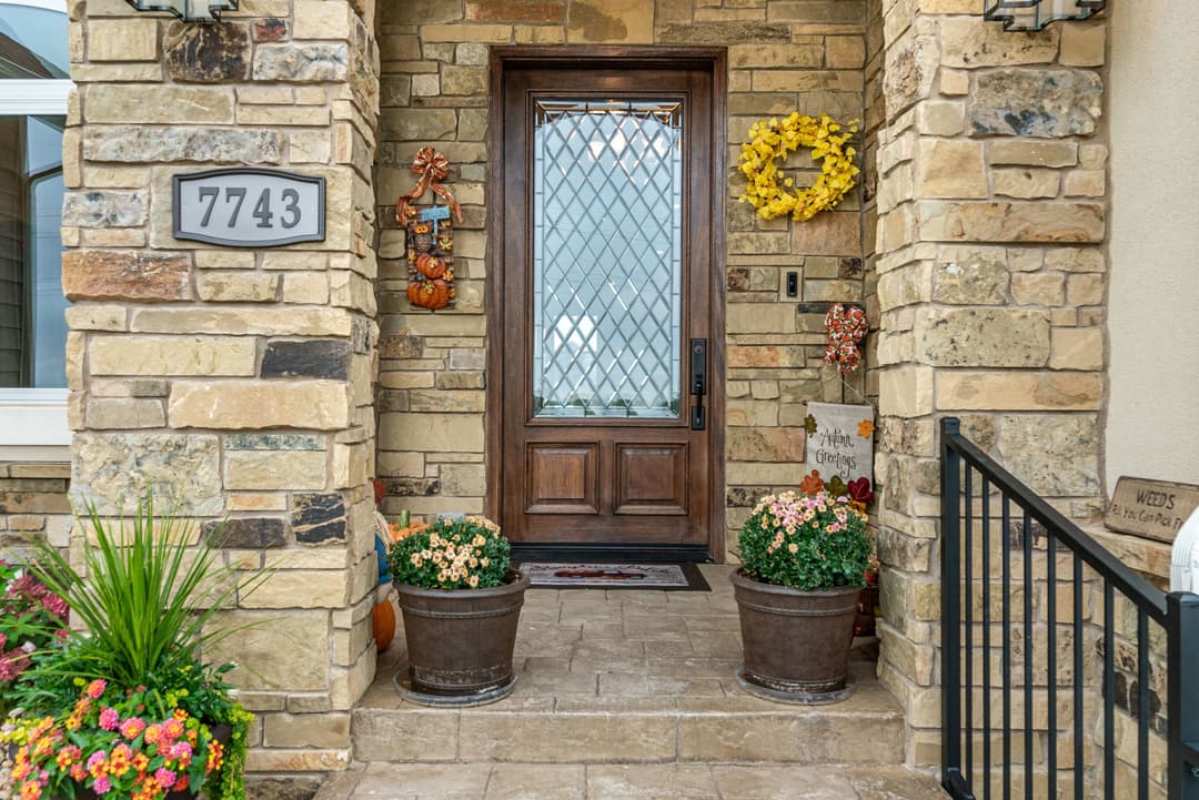 Welcoming stone entrance with a decorative door, plants, and fall-themed decor.