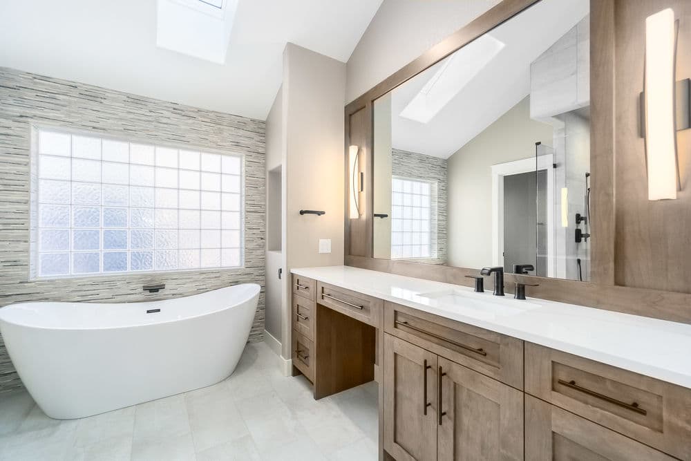 Modern bathroom with freestanding tub, wooden vanity, and large glass block window.