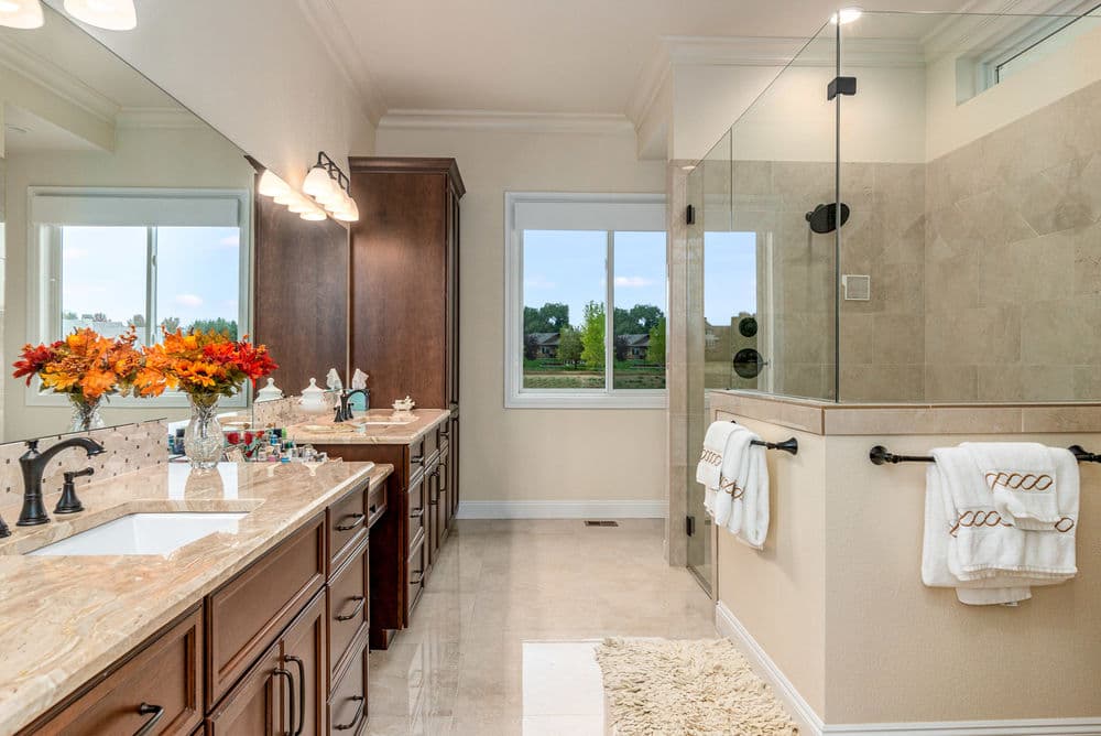 Luxurious modern bathroom with double sinks, glass shower, and scenic window view.