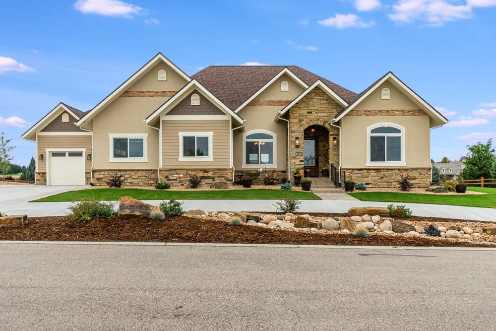 Modern family home with stone accents, manicured lawn, and spacious driveway on a clear day.