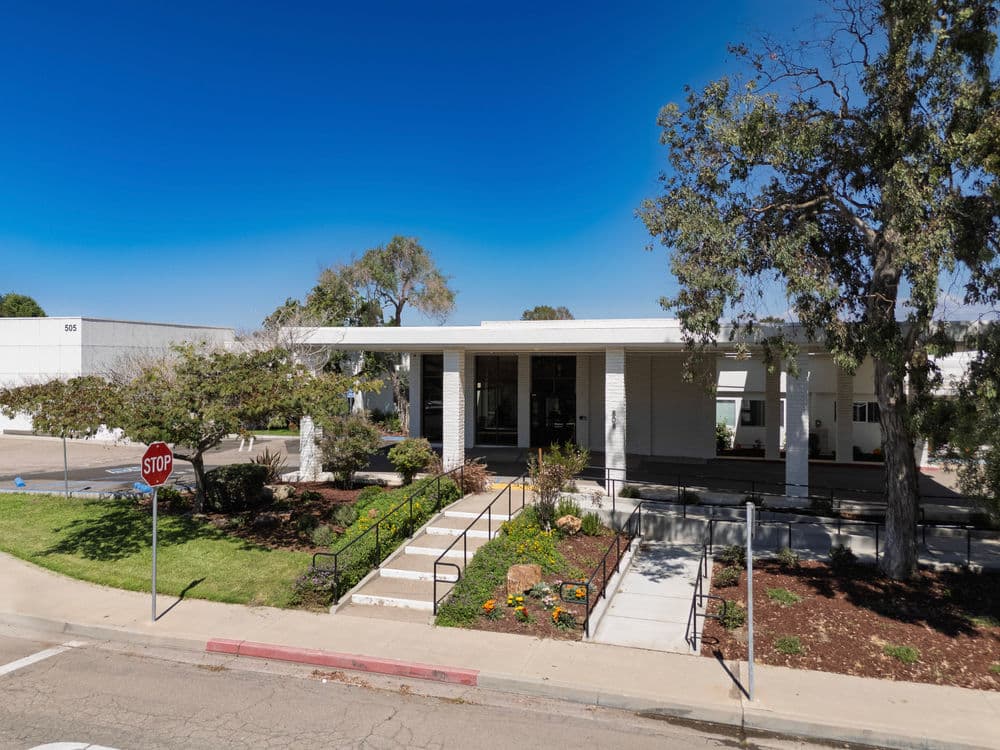 Modern building entrance with landscaped path, stop sign, and clear blue sky.
